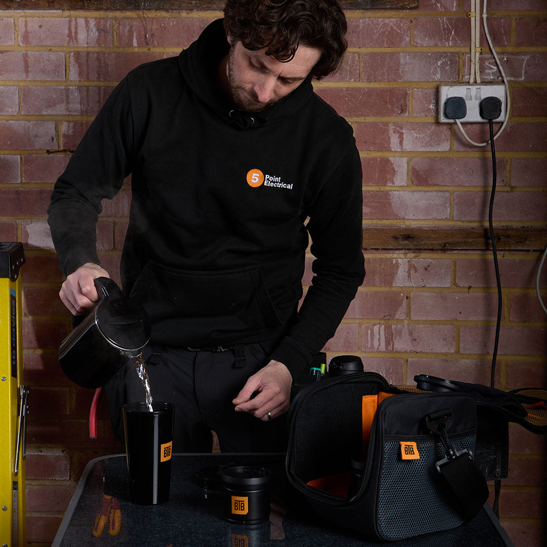 Tradesman pouring a cup of tea on site with a kettle and mug kit